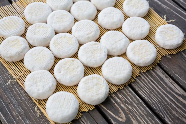 Multiple wheels of goat cheese on a straw mat
