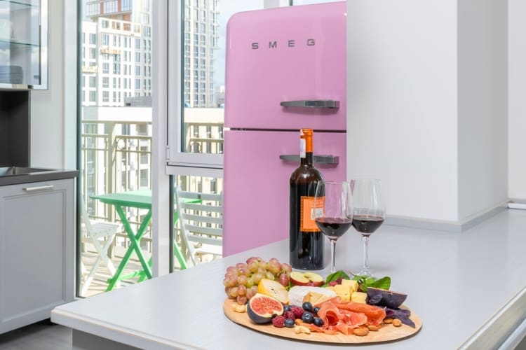 A bottle and glasses of red wine on a counter next to a pink fridge