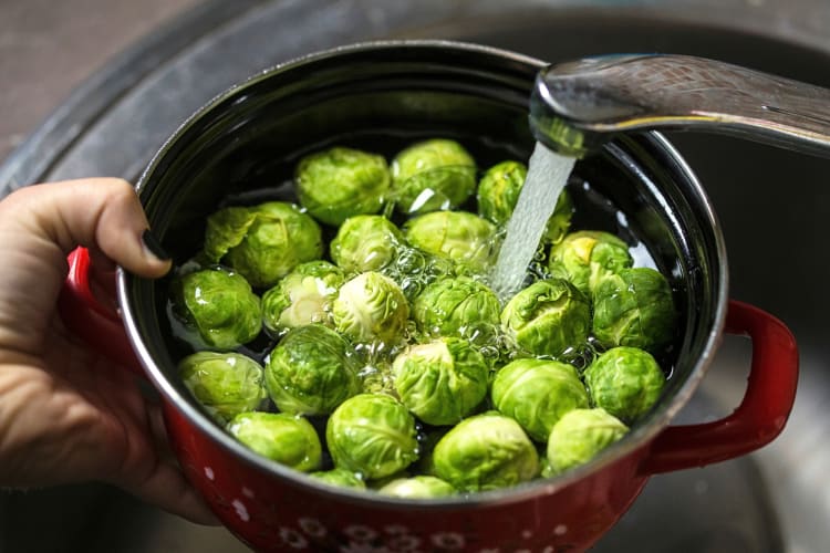Person's hand holding a pot with Brussels sprouts in them, being filled with water