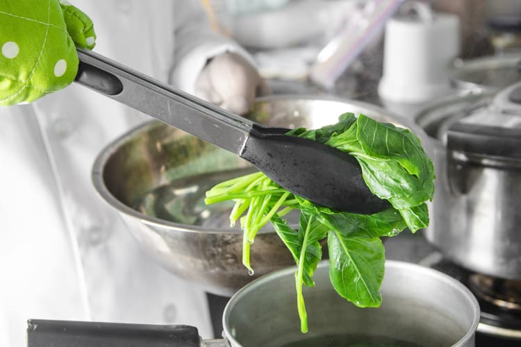 Chinese kale being transferred from boiling to ice water with tongs