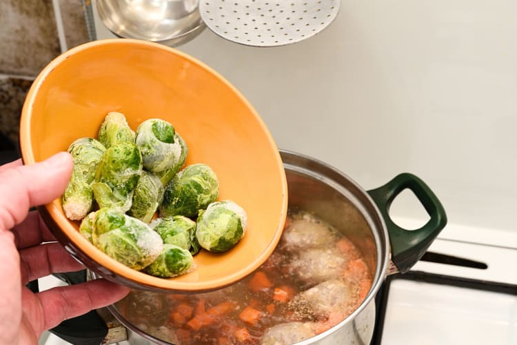 Person's hand pouring frozen Brussels sprouts from a bowl into a pot of boiling water