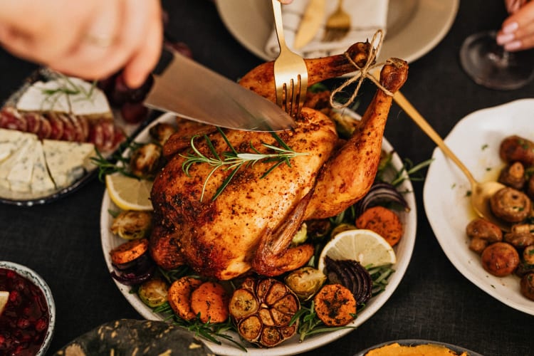 Full chicken in a bowl of cooked vegetables being cut