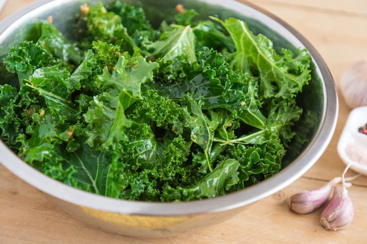 Kale leaves in a steel bowl next to garlic cloves