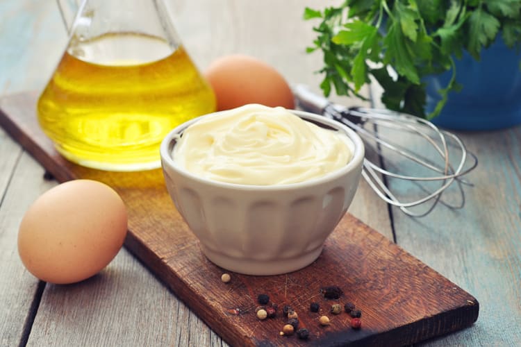 Homemade mayonnaise in a bowl, in front of two eggs and olive oil