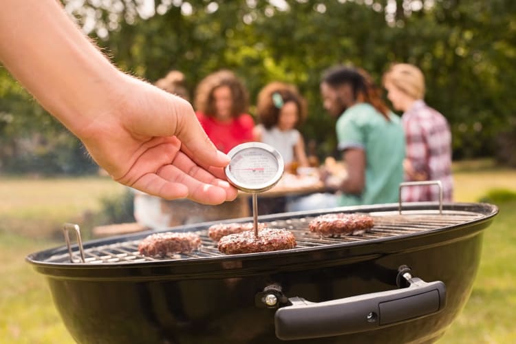 Person's hand measuring burger patty temperatures on a barbeque