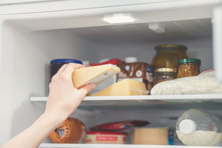 Person's hand placing wrapped cheese in a fridge