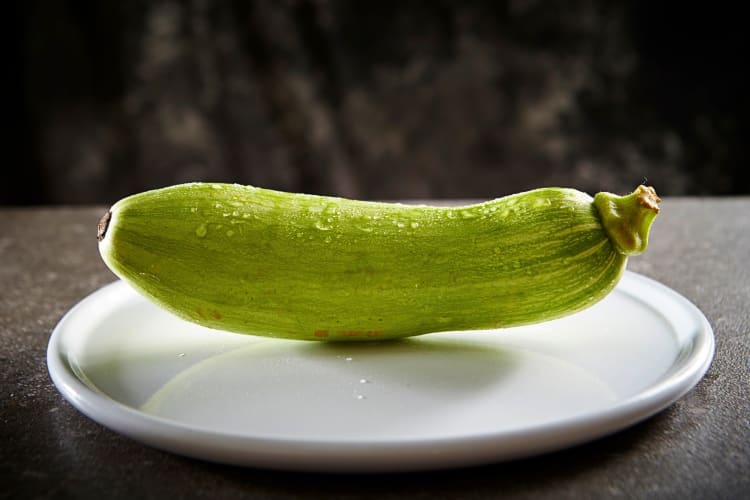 Whole zucchini with water drops on it sitting on a plate