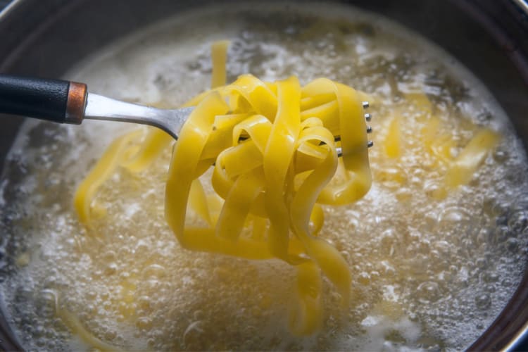 Tagliatelle pasta that's cooking being lifted from water with a fork