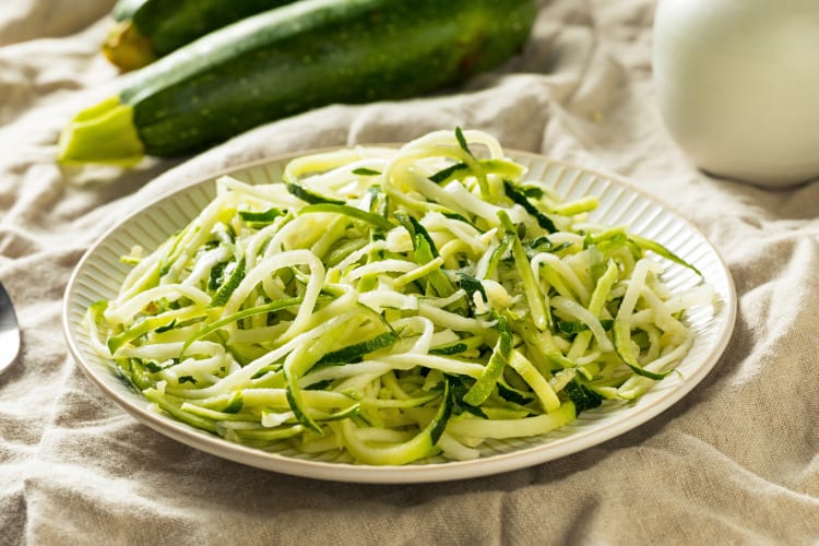 Zucchini noodles on a plate in front of two whole zucchini