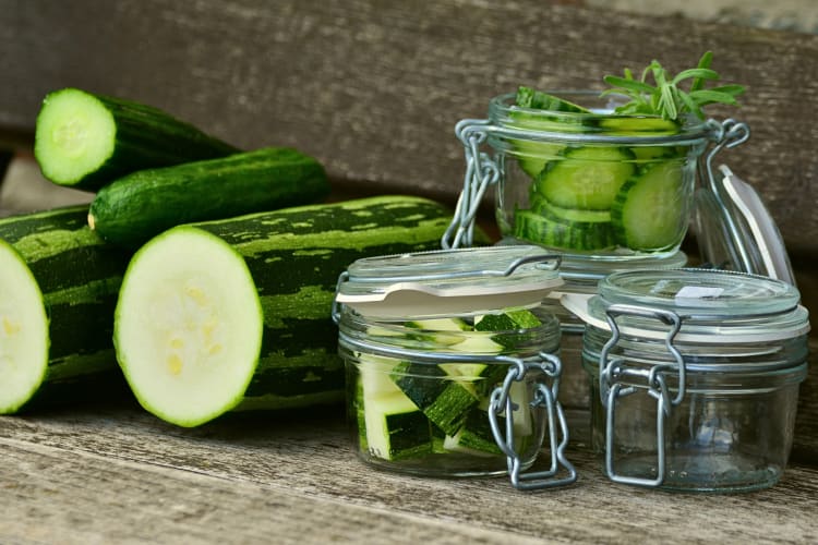 Zucchini slices and cubes in jars next to empty jars and larger portions of zucchini