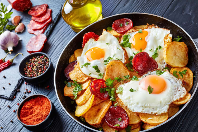Huevos rotos on a plate next to spices and sliced meat