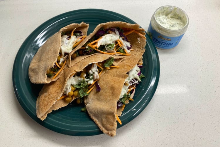 Wholewheat pita pockets with filling on a green plate next to a jar of tzatziki