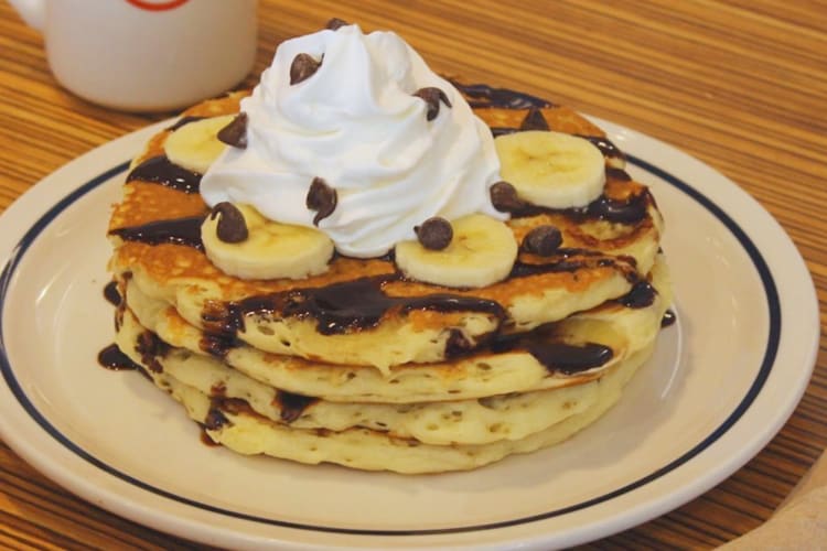 A stack of pancakes with bananas and whipped cream