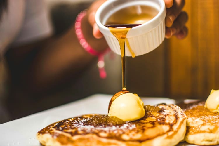 A person pouring syrup on pancakes