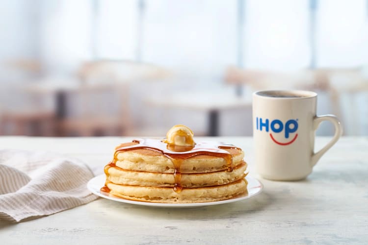 Eye-level view of three pancakes covered in syrup, next to a mug, from IHOP