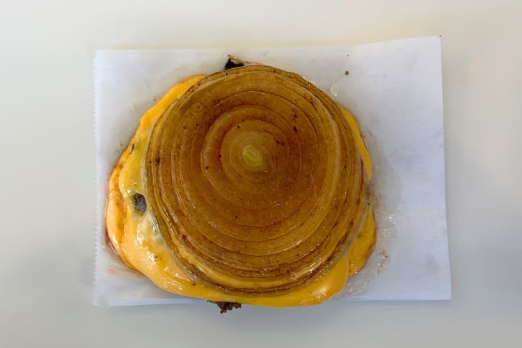 A burger patty and cheese between grilled onion slices