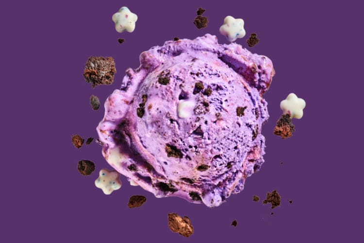 A scoop of purple ice cream surrounded by chocolate cookie chunks and white chocolate stars
