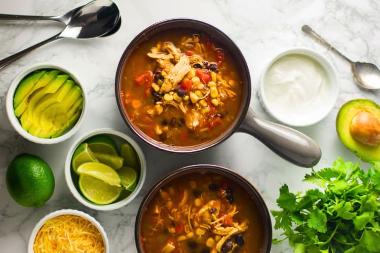 Bowls of tortilla soup surrounded by ingredients 
