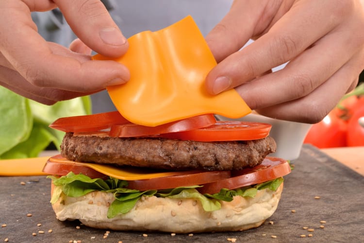 Close-up of a person's hands placing a slice of cheese on a burger