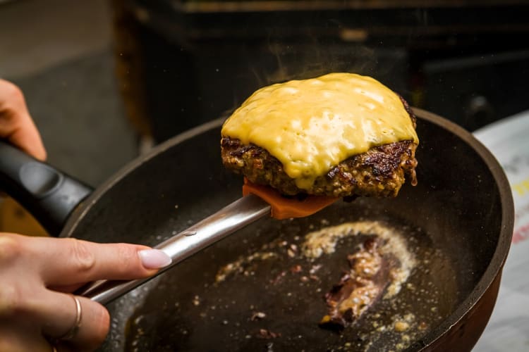Person's hand holding a spatula with a patty covered in cheese