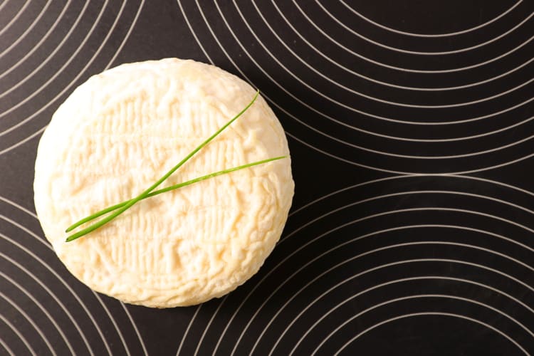 Aerial shot of a wheel of goat cheese on a black background