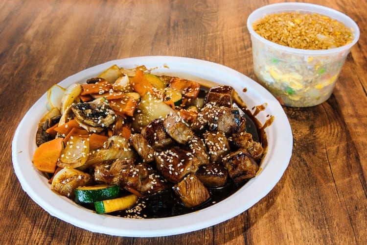 Hibachi-style steak and vegetable dish, next to a container of rice