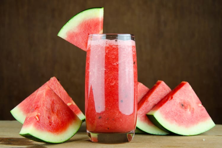 A glass of watermelon juice next to fresh watermelon slices