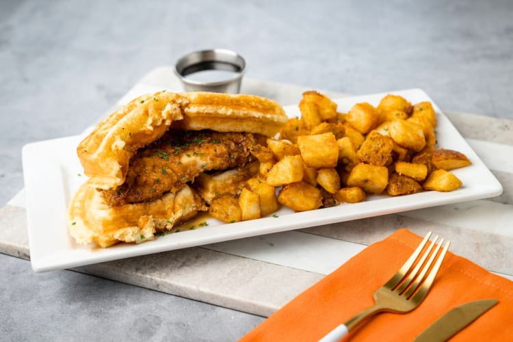 A chicken and waffle sandwich with home fries