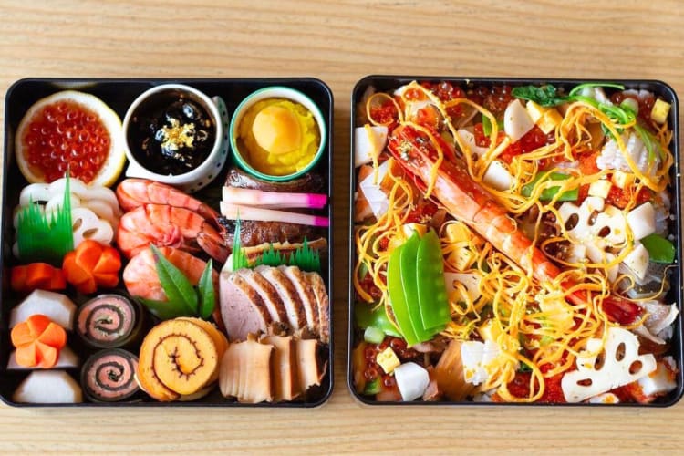 Two bento boxes with sushi, seafood and noodles