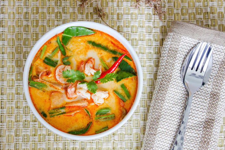 Aerial view of a tom yum soup and a fork and spoon on a napkin