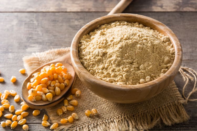 cornflour in bowl on wooden surface next to corn kernels