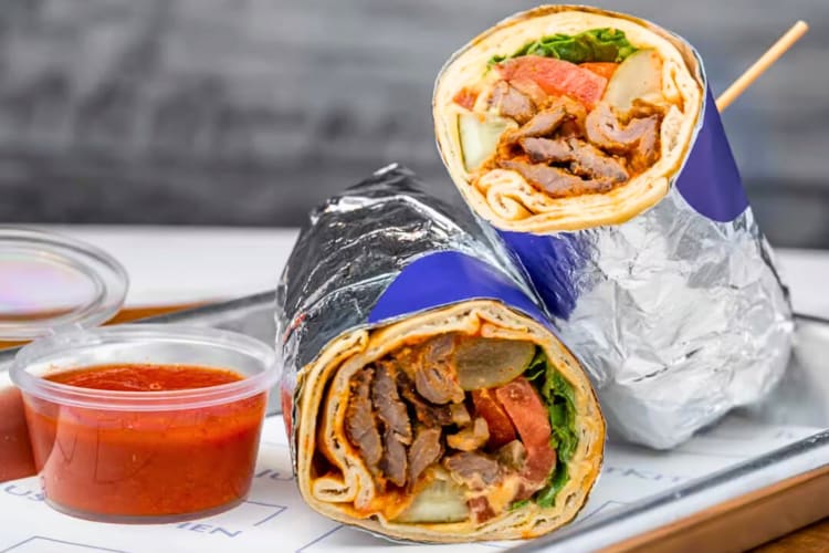 Meat shawarma wrapped in foil with a side sauce, from Just Kitchen 