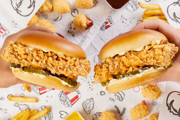 Two people holding chicken sandwiches from KFC