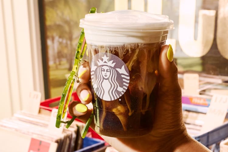 A person holding a Starbucks drink with coffee and creamer