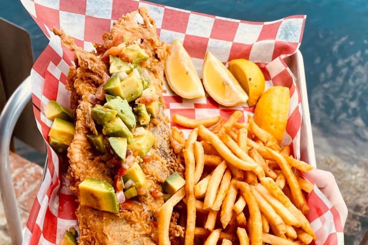 Battered fish, chips, lemon wedges and avocado on red and white checkered paper