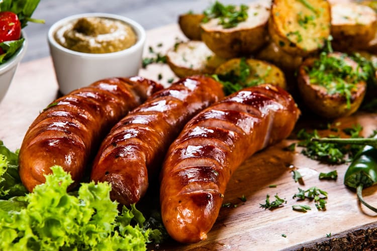 Three kielbasa sausages on a board with dipping sauce, bread and salad.