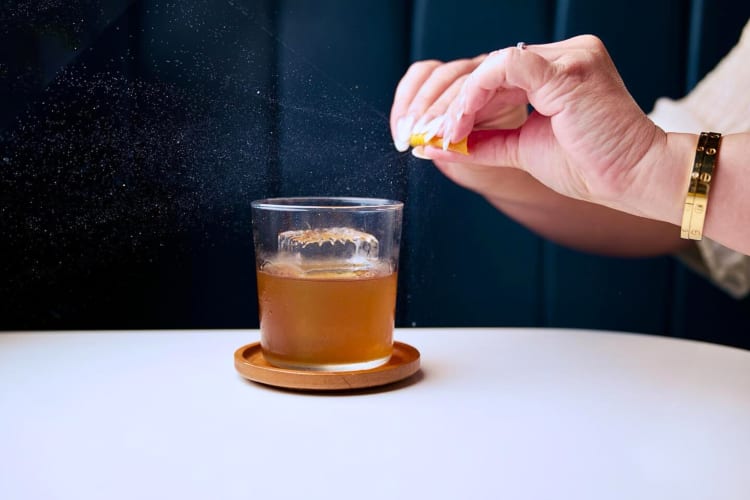 Person's hands squeezing a lemon peel over a cocktail