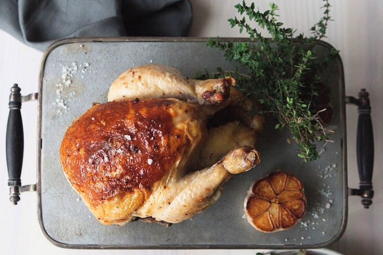 Aerial view of a roast chicken on a tray with garlic and herbs, from Kinship
