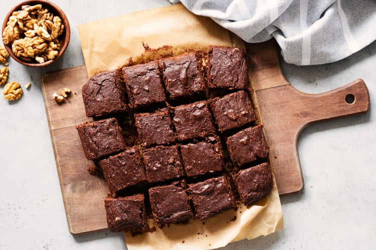 16 Brownies on a chopping board next to a bowl of walnuts