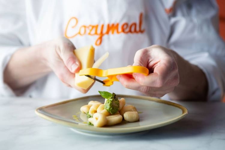 A person grating cheese onto gnocchi 