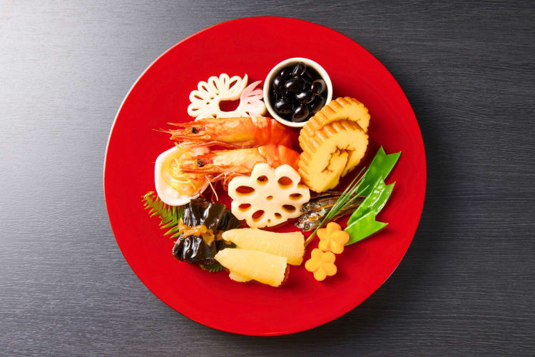 A red plate with shrimp, rolled omelette and other Japanese foods