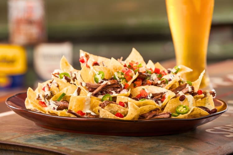 A plate of nachos with steak next to a beer