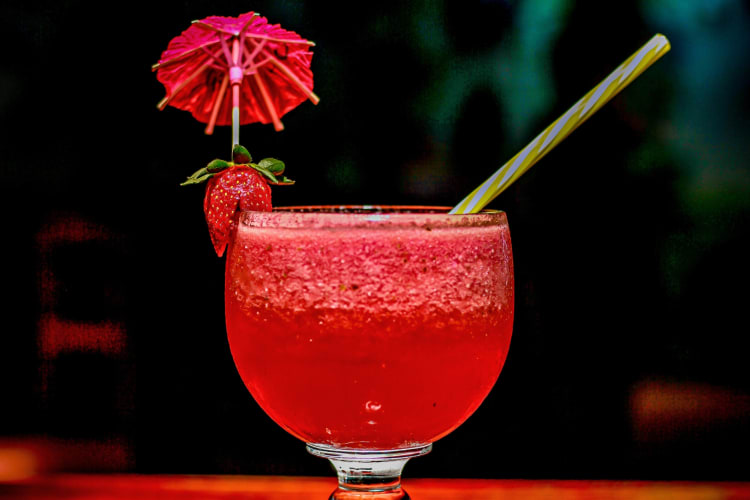 A red drink with a strawberry and cocktail umbrella