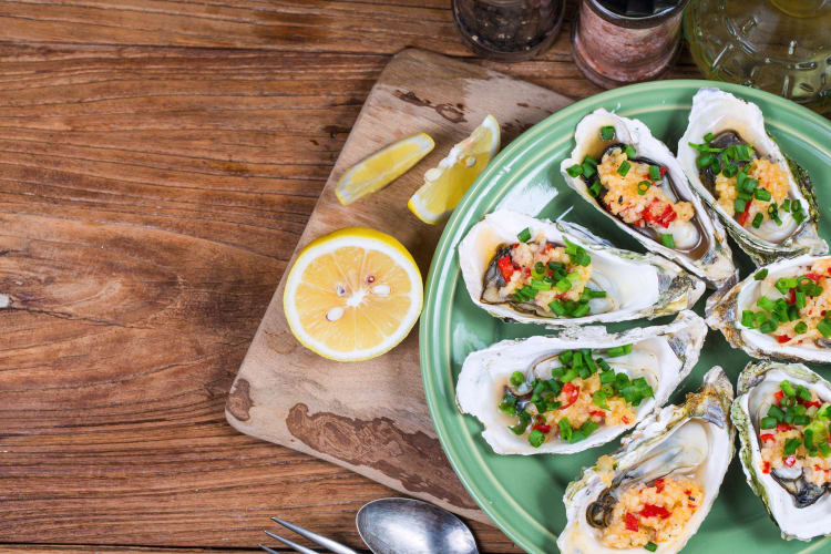 Seven oysters on a plate with lemon wedges on the side