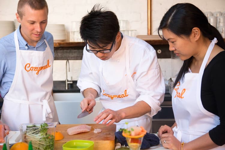 An expert chef overseeing two people in a cooking class