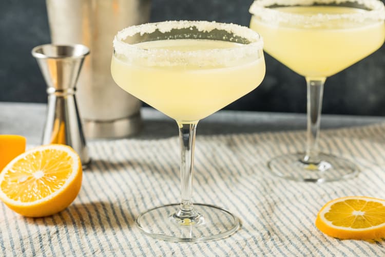 Two lemon drop martinis, orange slices and a shot pourer, on a dish cloth