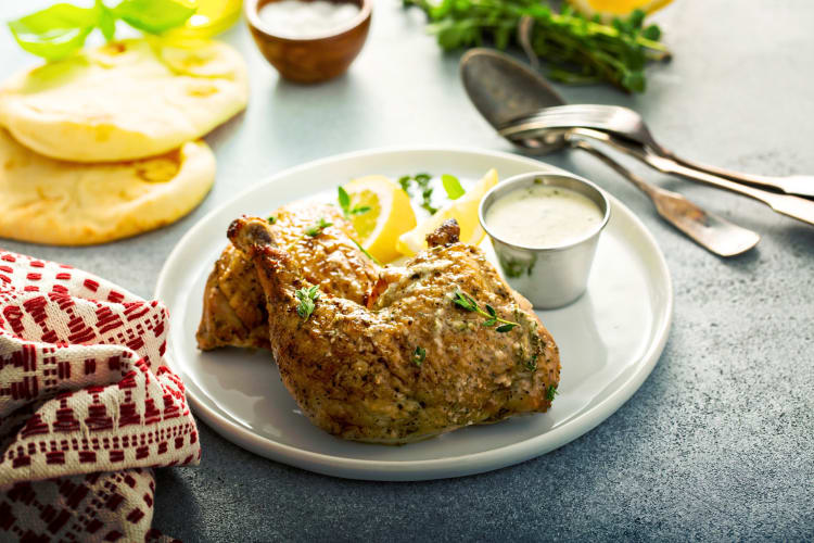 Lemon-herb airline chicken on a plate with lemon wedges and a small container of sauce