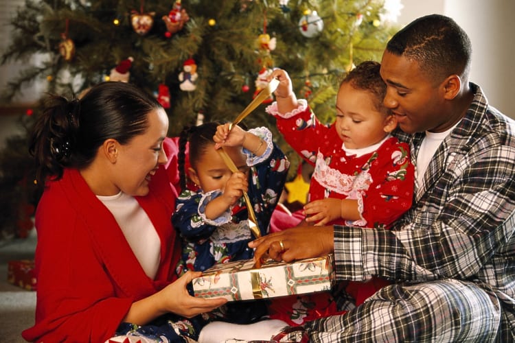 A mother, father and two daughters opening a present together as a Christmas family tradition