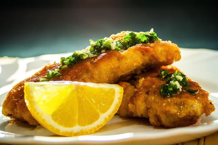 Two pieces of fried fish with garnish and a lemon wedge