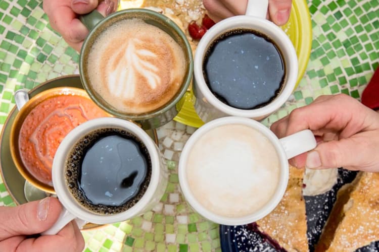 Aerial shot of four hands clinging mugs together with warm drinks in them